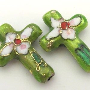 May include: Two green cross-shaped beads with white floral designs and red centers. The beads have gold accents and a glossy finish. The crosses are likely for jewelry making or religious crafts.