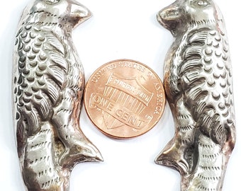 May include: Two silver-toned bird pendants with detailed feather and eye designs. Each pendant has a small loop at the top for hanging. A penny is placed between the pendants for size comparison. The pendants are on a white background.