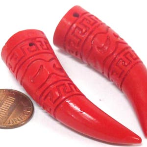 May include: Two red carved horn-shaped pendants with intricate designs. The pendants are about the size of a US penny.
