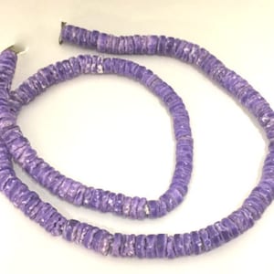 May include: A necklace composed of small, flat, round beads in shades of lavender and white. The beads are strung together, forming a flexible strand. The necklace is displayed against a white background, showcasing its color and texture.