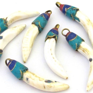 May include: Seven ivory-colored pendants with decorative caps. The caps are adorned with turquoise, blue, and red enamel, accented with gold-colored metal. Each pendant has a small loop for hanging.