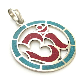 May include: Silver-tone pendant with an Om symbol. The pendant features a red Om symbol in the center, surrounded by a turquoise border. The pendant is designed with a loop for a chain.