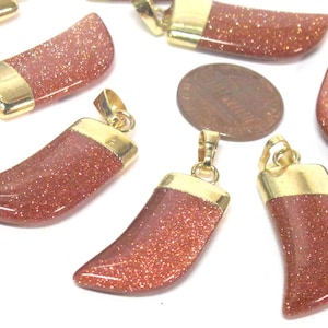 May include: Several goldstone pendants with gold-colored metal caps and loops. The pendants are a reddish-brown color with sparkling inclusions. A penny is included for size comparison. The pendants are on a white background.