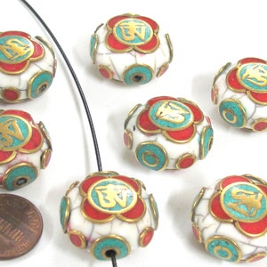 May include: A collection of white, round beads with a floral design. Each bead features red and turquoise accents, gold-colored trim, and a gold-colored symbol. The beads are strung on a black cord. A penny is included for size reference.