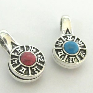May include: Two silver pendants with a circular design and a gemstone center. One pendant has a red gemstone, the other a blue gemstone. The pendants have a loop at the top for a chain.