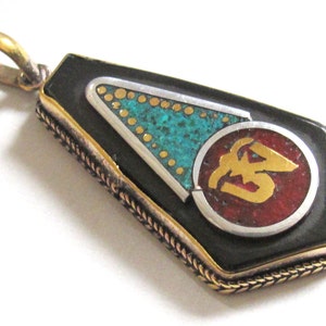 May include: A rectangular pendant with a black base, gold trim, and a gold bail. The pendant features a turquoise triangle, gold dots, and a red circle with gold lettering. The edges have a braided design.