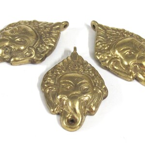 Puede incluir: Tres colgantes de lat&oacute;n con forma de cabeza de elefante estilizada. Los colgantes son de color dorado c&aacute;lido y presentan rasgos faciales detallados, incluyendo una trompa, ojos y orejas. Cada colgante tiene un peque&ntilde;o agujero para ensartar.