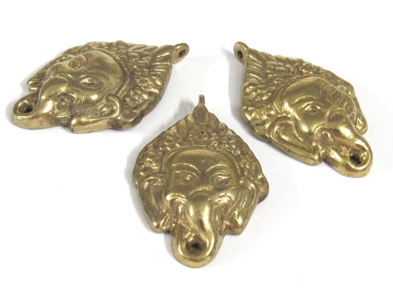 Puede incluir: Tres colgantes de lat&oacute;n con forma de cabeza de elefante estilizada. Los colgantes son de color dorado c&aacute;lido y presentan rasgos faciales detallados, incluyendo una trompa, ojos y orejas. Cada colgante tiene un peque&ntilde;o agujero para ensartar.