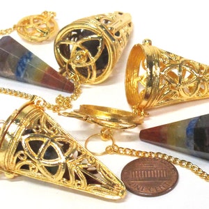 May include: Set of three gold-tone metal pendulum cages with a seven chakra crystal point pendulum. The cages feature a Celtic knot design and are open at the top. The pendulum is approximately 1.5 inches long.