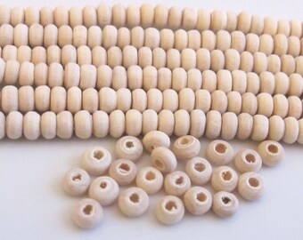 May include: Close-up of natural wood beads. The beads are cylindrical with a hole through the center. The beads are a light beige color and are arranged in rows and scattered. Ideal for jewelry making and crafts.