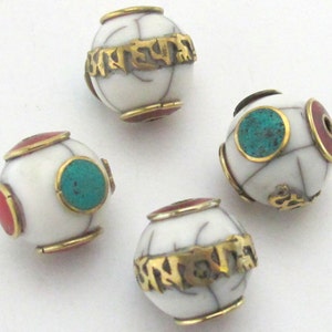 May include: Four white, spherical beads with gold-colored bands and inscriptions. Each bead has red and turquoise accents. The beads are likely for jewelry making or crafting.