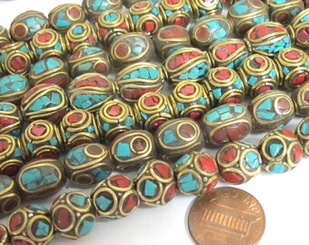 May include: Close-up of a collection of handcrafted beads. The beads feature a combination of red and turquoise stone inlays, set within a brass-colored metal frame. The beads have a unique, textured appearance, and are likely for jewelry making.