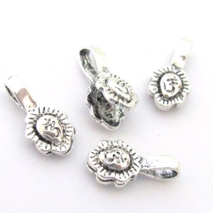 May include: Four small, silver-colored pendants with a floral design around a central Om symbol. Each pendant has a loop at the top for attaching to a chain or other jewelry component. The pendants are displayed on a white background.