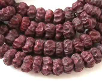 May include: Close-up of a strand of dark burgundy-colored beads. The beads have a textured, organic appearance, with a ridged surface. The beads are strung together, suggesting they are for jewelry making or crafting.
