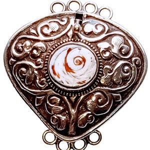 May include: Ornate silver-toned pendant with a central, circular design featuring a white and orange spiral pattern. The pendant has a detailed, embossed floral and scrollwork design, with loops at the top and bottom for attachment.