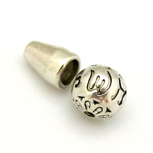 May include: A silver magnetic clasp with a cylindrical barrel and a decorative sphere. The sphere features cut-out designs and is separated from the barrel, resting on a white background.