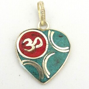 May include: Heart-shaped pendant with a silver bail. The pendant features a red circle with a gold Om symbol, surrounded by turquoise-colored stone and silver accents. The pendant is designed with a silver border.