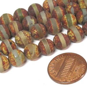 May include: Strand of round, natural stone beads with a brown, yellow, and gray striped pattern. A penny is included for size reference. The beads are approximately 0.75 inches in diameter.