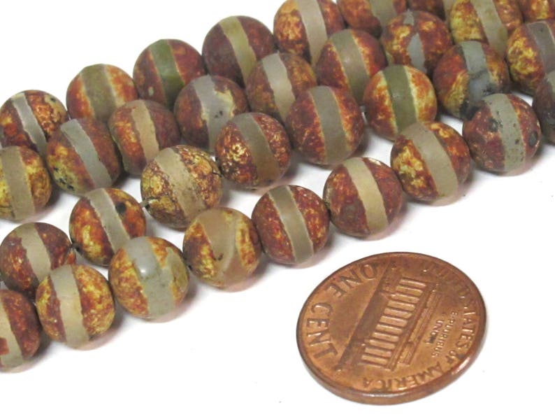 May include: Strand of round, natural stone beads with a brown, yellow, and gray striped pattern. A penny is included for size reference. The beads are approximately 0.75 inches in diameter.