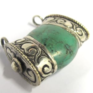 May include: A turquoise-colored pendant with silver-colored metal accents. The pendant has a barrel shape with ornate scrollwork and a small loop at the top for a chain. The metal has a gold-colored trim.