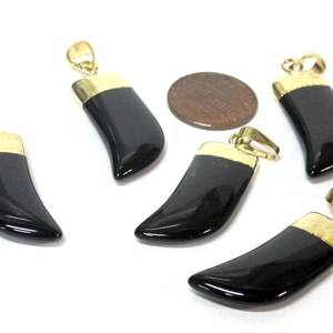 May include: Five black horn-shaped pendants with gold-colored caps and loops. A penny is also present. The pendants are glossy and appear to be made of a smooth, dark material. The gold caps add a touch of elegance.