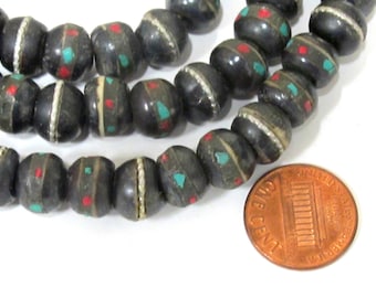 May include: Strands of dark gray beads with inlaid red and turquoise accents. Each bead has a white band around the center. A US penny is included for size reference.