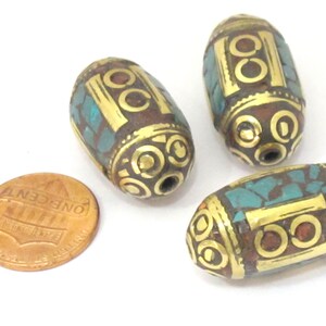 May include: Four decorative, barrel-shaped beads. The beads are brown with gold-colored metal accents and turquoise-colored stone inlays. The beads have a hole drilled through the center. A U.S. penny is next to the beads for size comparison.