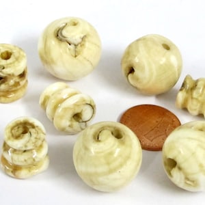 May include: A collection of ivory-colored beads in various shapes, including spheres, stacked cylinders, and spiral designs. The beads have a marbled appearance with brown and tan swirls. A small, brown coin is also present.