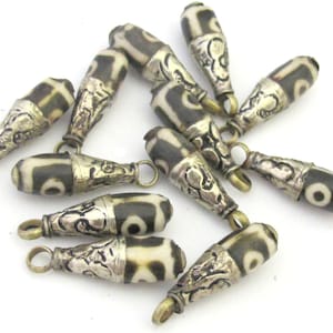 May include: A collection of cylindrical dzi beads with a black and white pattern. Each bead has a silver-colored metal cap with ornate detailing and a small loop for stringing.