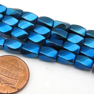 May include: Close-up of several strands of shiny, blue-colored, faceted beads. The beads are a deep, metallic blue with a reflective surface. A US penny is included for size comparison, showing the beads' small size. These beads are suitable for jewelry making.