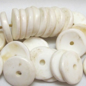 May include: A collection of off-white, disc-shaped beads with a central hole, some strung together. The beads vary in size and have a slightly aged appearance. The beads are likely for jewelry making or crafts.
