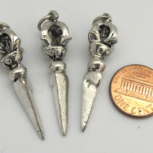 May include: Three silver-colored metal pendants with a detailed floral design at the top and a pointed, dagger-like shape. A US one-cent coin is next to the pendants for size comparison. The pendants have a loop at the top for hanging.