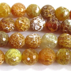 May include: Close-up of a strand of round, crackled beads in shades of yellow, orange, and brown. The beads have a textured, web-like pattern across their surface. The beads are strung together, suggesting they are for jewelry making or crafts.