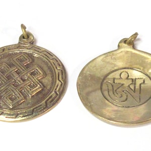 May include: Two brass pendants. One pendant features an intricate, geometric knot design within a circular frame. The other pendant has an oval shape with an Om symbol. Both pendants have a small loop for a chain.