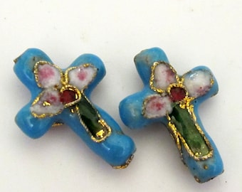May include: Two turquoise blue cross-shaped pendants. Each cross features a floral design with pink and white petals, a red center, and green leaves, all outlined in gold. The crosses are likely for jewelry or craft projects.