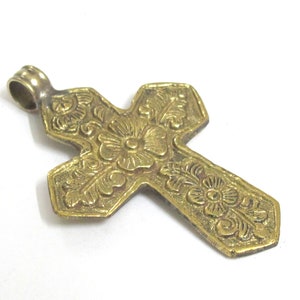 May include: A detailed, gold-colored cross pendant with floral and scrollwork designs. The cross has a loop at the top for a chain. The pendant is likely made of brass or a similar metal. The cross is a religious symbol.