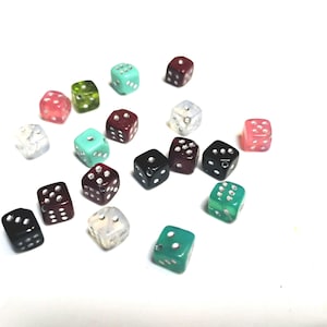 May include: A collection of colorful dice scattered on a white surface. The dice are various colors, including red, green, black, and pink. Each die has white dots indicating the numbers.