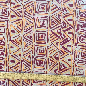 K&ouml;nnte beinhalten: Ein beigefarbener Stoff mit einem sich wiederholenden geometrischen Muster in Orange- und Burgunder-T&ouml;nen. Das Muster zeigt Dreiecke und Quadrate.