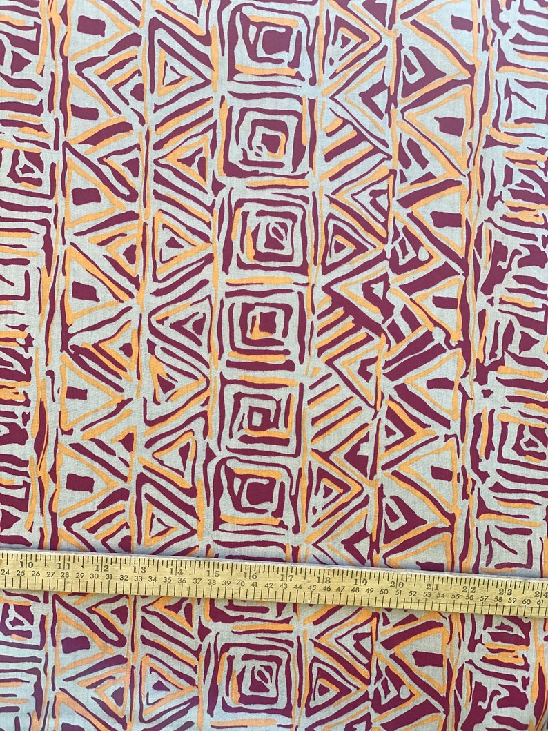 K&ouml;nnte beinhalten: Ein beigefarbener Stoff mit einem sich wiederholenden geometrischen Muster in Orange- und Burgunder-T&ouml;nen. Das Muster zeigt Dreiecke und Quadrate.