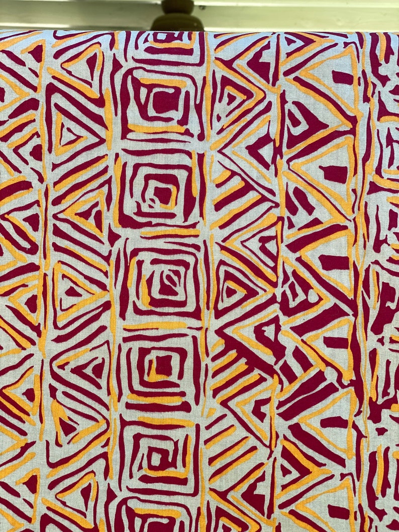 K&ouml;nnte beinhalten: Ein Stoff mit einem geometrischen Muster in den Farben Burgunderrot und Gold. Das Muster zeigt Dreiecke und Quadrate.