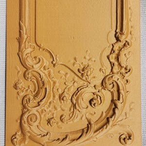 以下が含まれることがあります： 長方形のタン色の装飾パネル。浮き彫りの詳細なデザインで、アカンサスの葉、花のモチーフ、対称的な曲線が特徴です。クラシックでヴィンテージな美学を作り出しています。