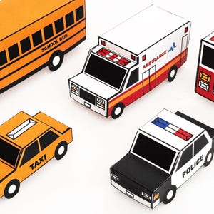 May include: A collection of paper craft vehicles including an orange school bus, a white ambulance with red stripes and the text AMBULANCE, a yellow taxi with the text TAXI, and a black and white police car with the text POLICE and a light bar.