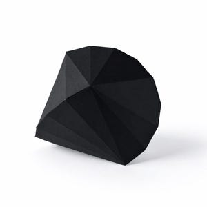 May include: A black, geometric paper box with a faceted design. The box is a dark matte black and has a unique shape with multiple angled surfaces. The box is on a white background.