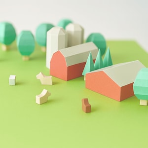 Puede incluir: Una escena de granja en miniatura de papel con graneros rojos, silos blancos y árboles verdes sobre una superficie verde. Pequeñas figuras de animales y sillas de color claro están dispersas alrededor de la granja. La escena es un diorama artesanal caprichoso.