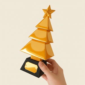 May include: A gold-colored Christmas tree trophy with a star on top. The tree is made of stacked triangular shapes and sits on a black base with a gold plaque. The trophy is held in a person's hand.
