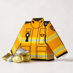 Puede incluir: Un recorte de papel amarillo de una chaqueta de bombero con rayas reflectantes plateadas, ribetes negros y un gráfico de radio. La chaqueta presenta un emblema circular en la manga y está acompañada por varios chocolates pequeños envueltos en papel aluminio.