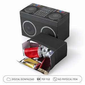 Könnte beinhalten: Eine schwarze rechteckige Schachtel mit einem aufgedruckten DJ-Controller-Motiv auf der Oberseite und zwei großen Lautsprechern auf der Vorderseite. Eine offene schwarze Schachtel im Vordergrund enthält mehrere rechteckige Gegenstände, die in rote, goldene und silberne Metallfolie eingewickelt sind.