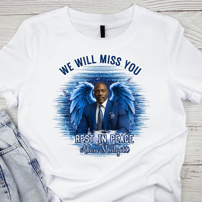 May include: White t-shirt with a graphic of a man in a blue suit, adorned with blue angel wings. The text "WE WILL MISS YOU" arches above the image, with "REST IN PEACE Alan Midgett" below.