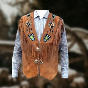 Könnte beinhalten: Braune Wildlederweste mit Fransen und Perlenverzierungen. Die Weste hat einen V-Ausschnitt und dekorative Perlen in verschiedenen Farben. Sie wird über einem gestreiften Button-Down-Hemd getragen und erzeugt einen Lagen-Look.