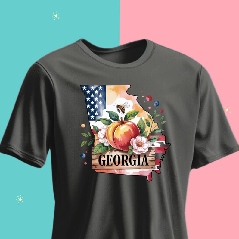 May include: Dark gray t-shirt featuring a watercolor design of the state of Georgia. The design includes a peach, flowers, a bee, and the text "GEORGIA" on a wooden sign. The top left corner features the American flag.